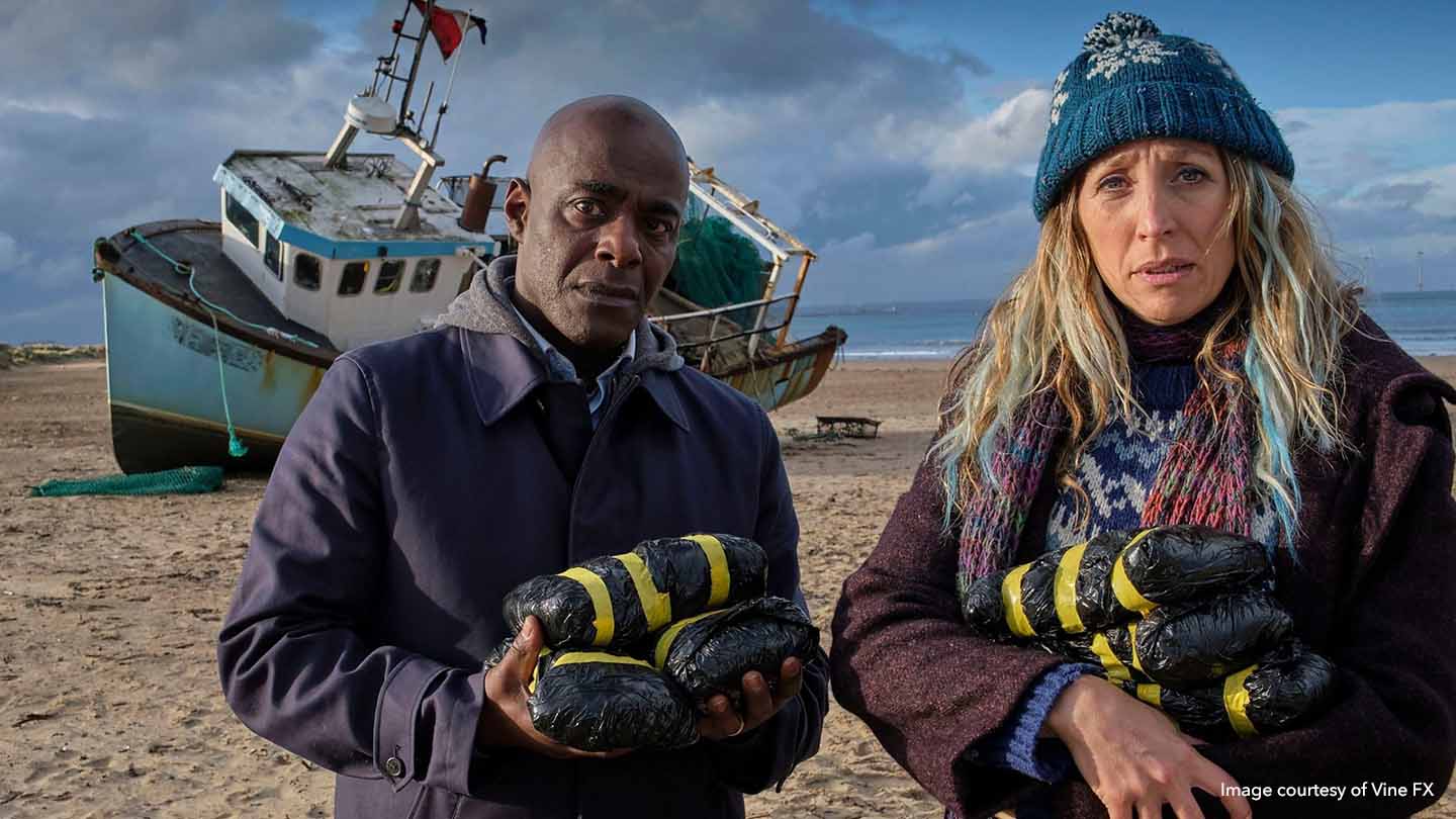 Paterson Joseph as Samuel, and Daisy Haggard as Janet, standing on beach in front of grounded boat in still from BBC’s Boat Story