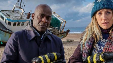 Paterson Joseph as Samuel, and Daisy Haggard as Janet, standing on beach in front of grounded boat in still from BBC’s Boat Story